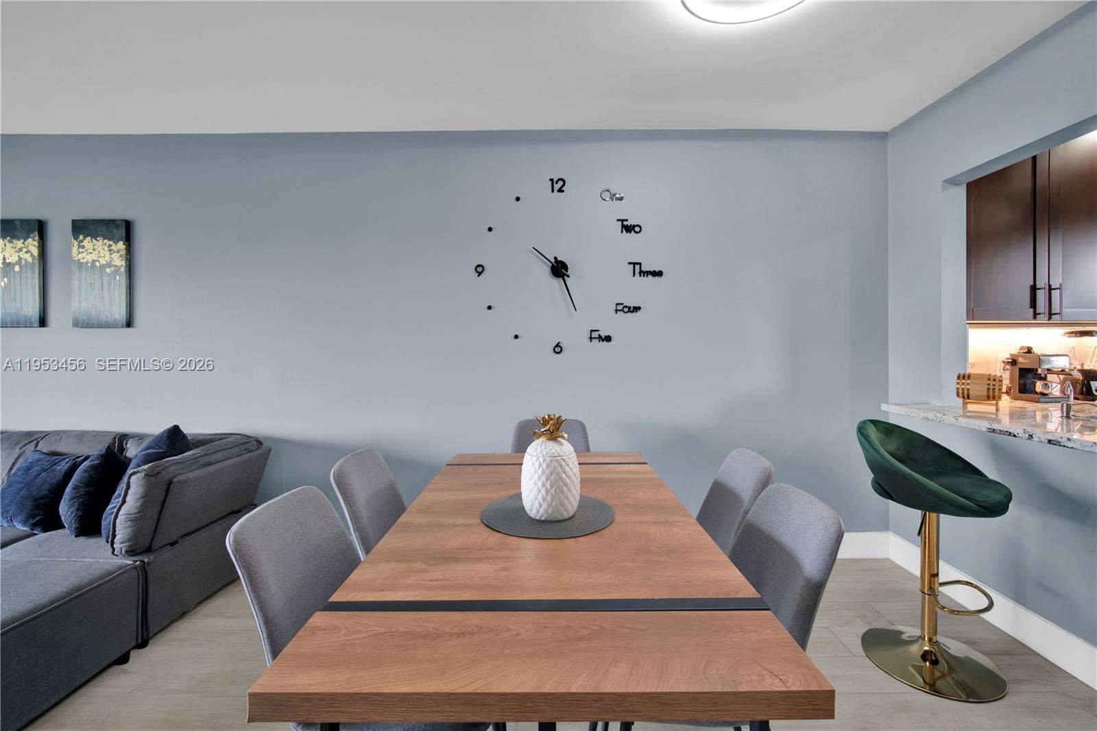 A dining area features a wooden table, gray chairs, and a wall-mounted clock — 950 Hillcrest Dr # 414, Hollywood FL 33021, HOLLYWOOD, FL