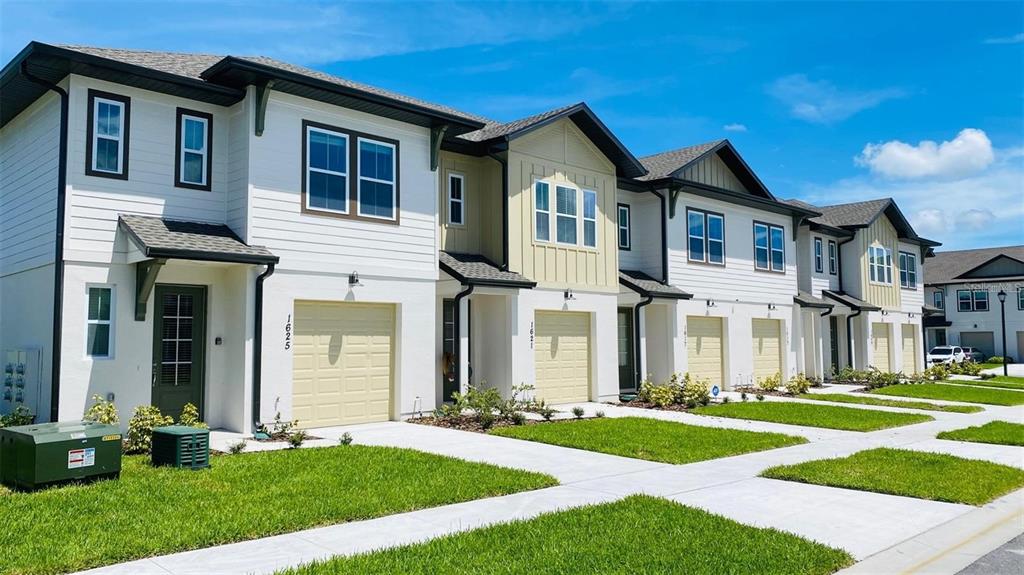 A row of modern two-story townhouses with white siding, tan garage doors, and green front doors — 1621 PELICAN DRIVE, DAVENPORT, FL