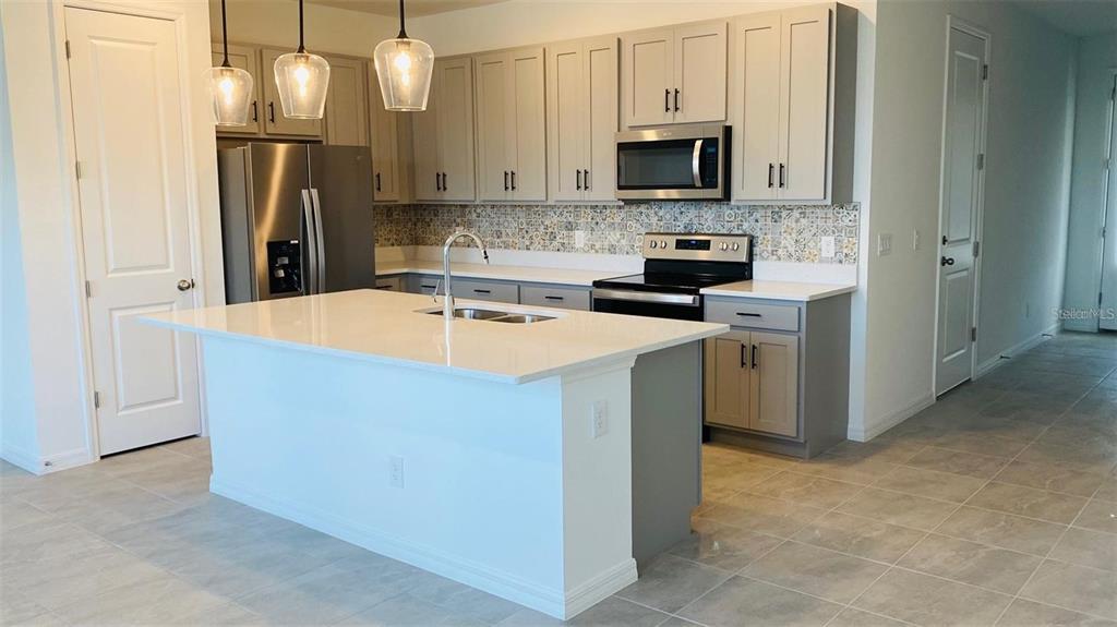 A kitchen features gray cabinets, a white quartz island, and a patterned tile backsplash — 1621 PELICAN DRIVE, DAVENPORT, FL