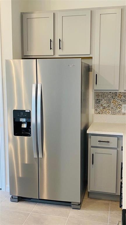 A stainless steel side-by-side refrigerator stands next to gray kitchen cabinets and a tiled backsplash — 1621 PELICAN DRIVE, DAVENPORT, FL