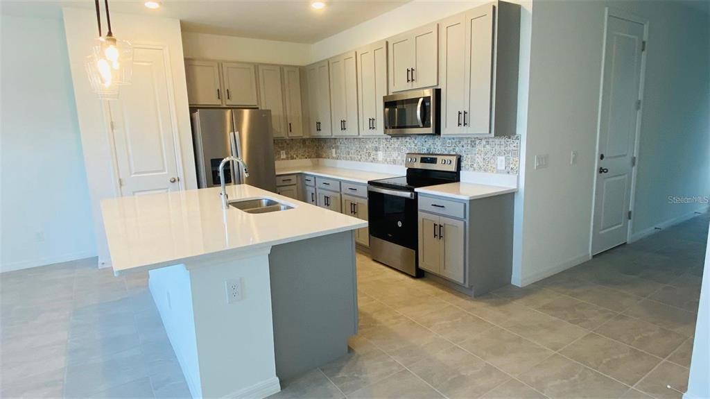 A kitchen features gray cabinets, stainless steel appliances, a white island, and patterned tile backsplash — 1621 PELICAN DRIVE, DAVENPORT, FL