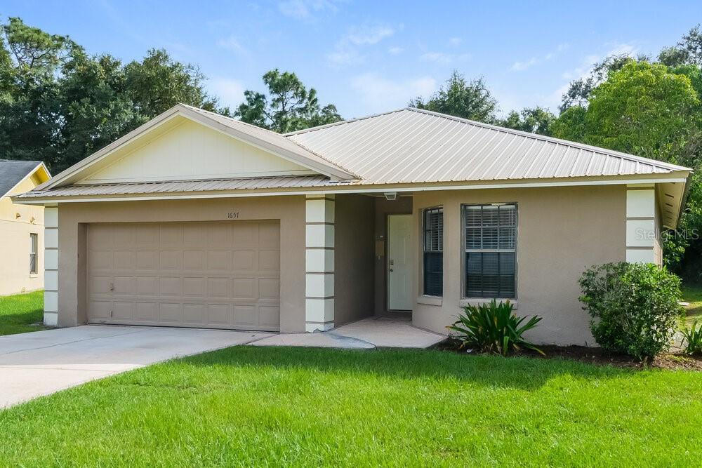 A single-story house with a tan stucco exterior, metal roof, and a two-car garage — 1657 SUNBURST WAY, KISSIMMEE, FL