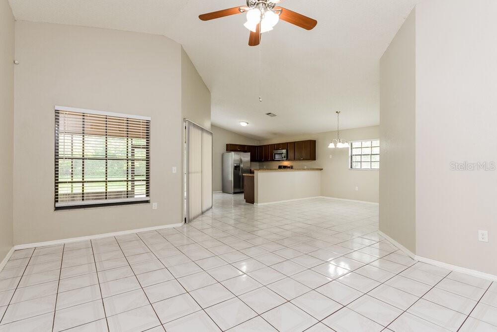 A bright, open-concept living area features white tile flooring, neutral walls, and a kitchen beyond — 1657 SUNBURST WAY, KISSIMMEE, FL