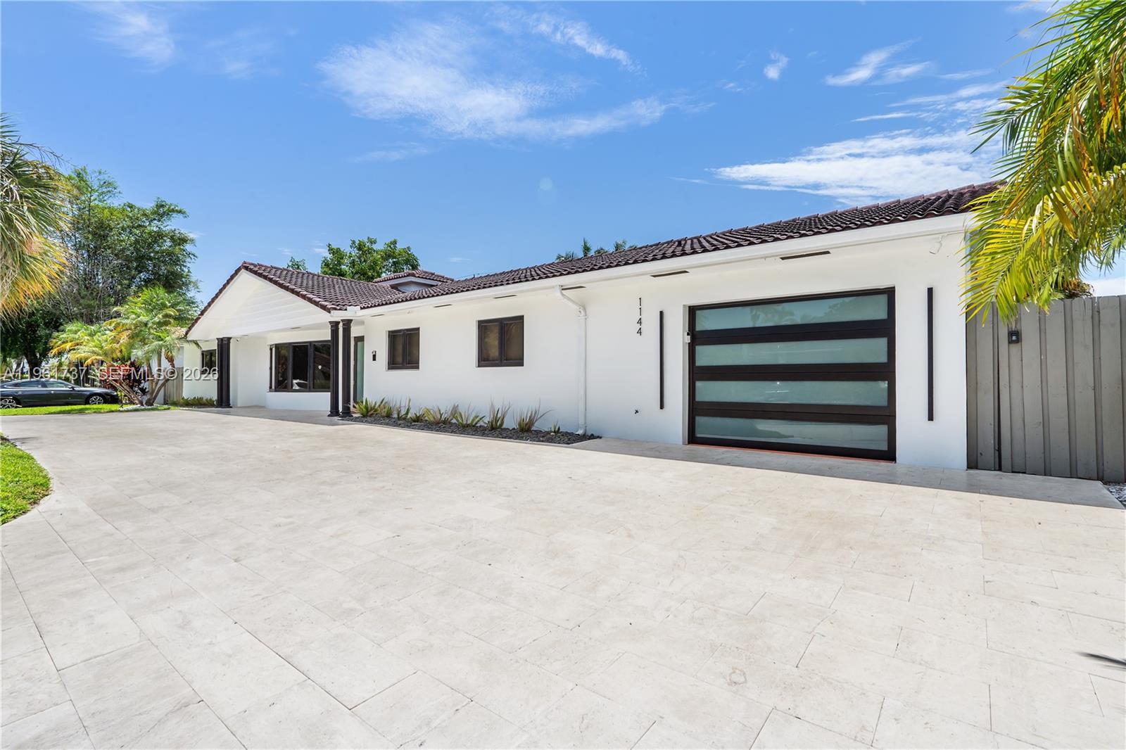 A white single-story house features a modern glass garage door and a large paved driveway — 1144 Adams St, Hollywood FL 33019, HOLLYWOOD, FL