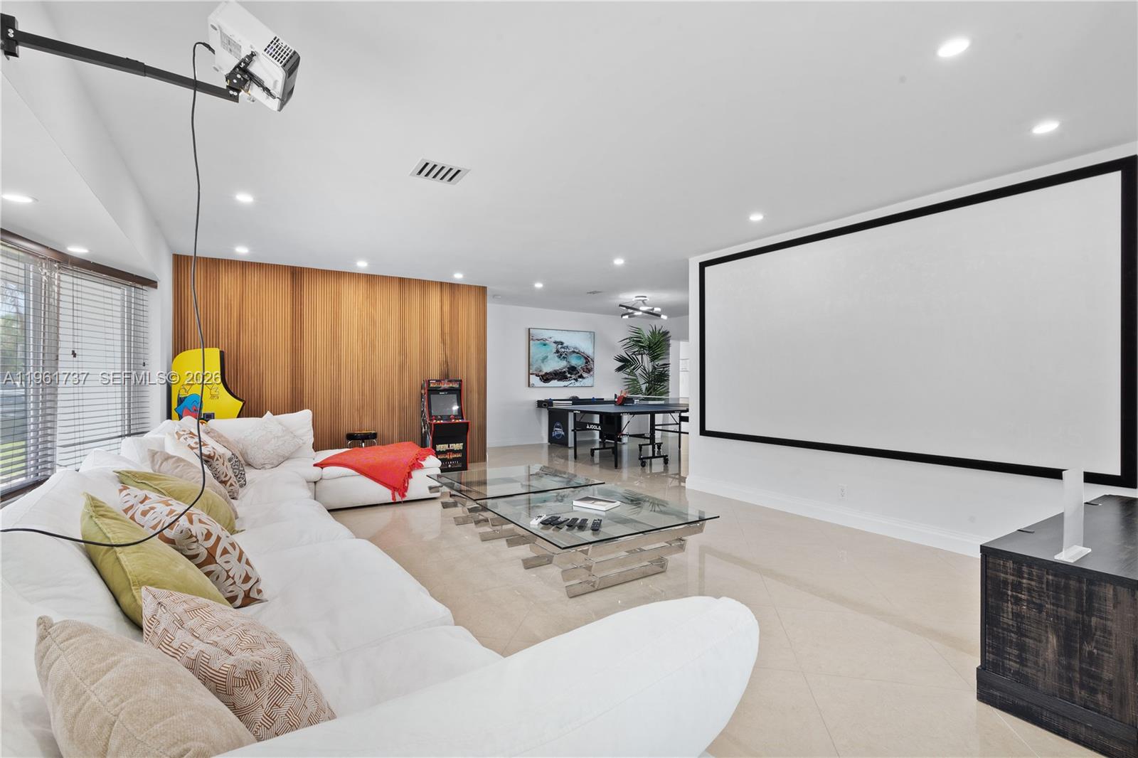 A spacious home theater room features a large projection screen, white sofa, and game area — 1144 Adams St, Hollywood FL 33019, HOLLYWOOD, FL
