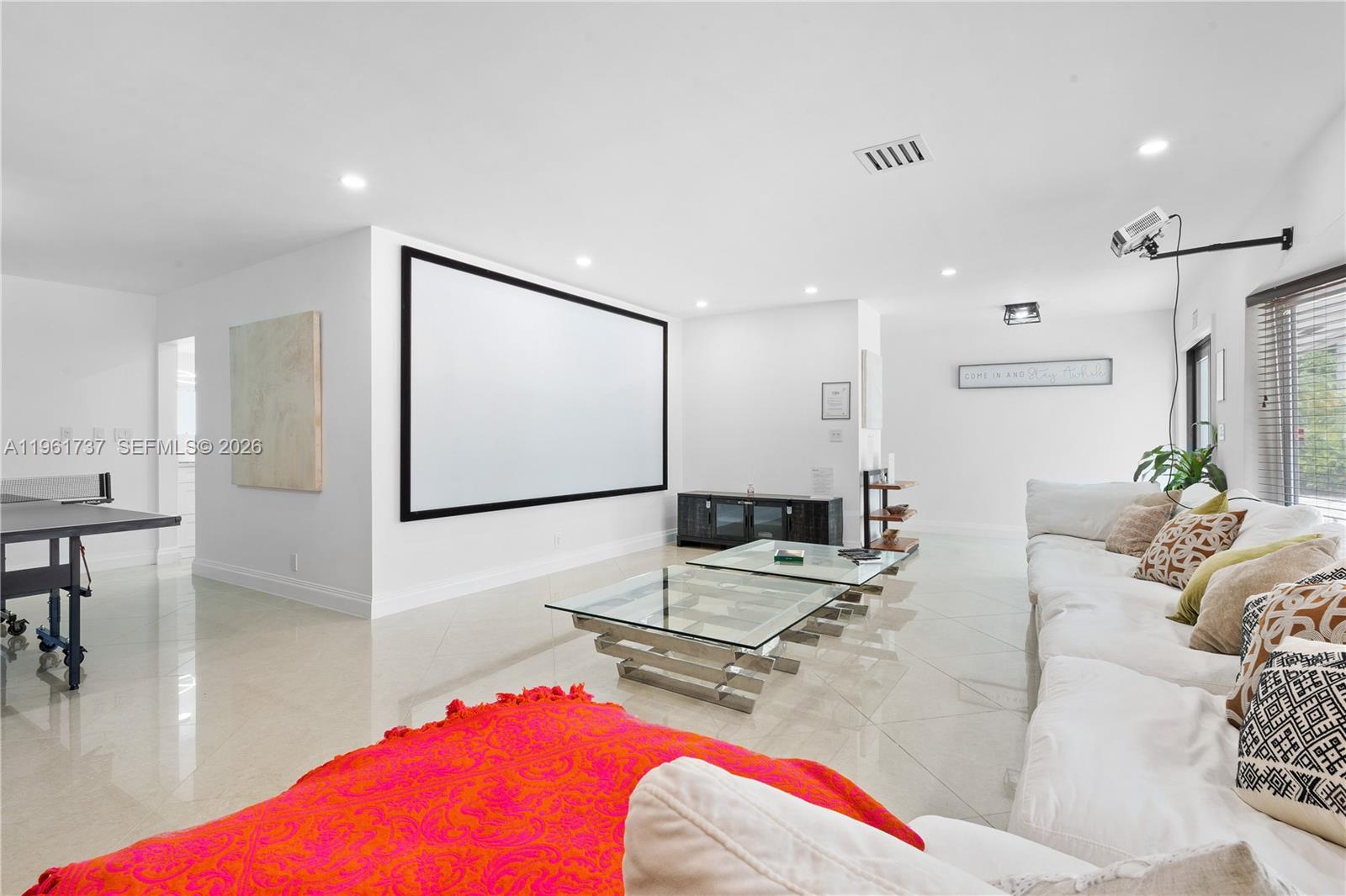 A bright living room features a large projector screen, glass coffee tables, and white sofas — 1144 Adams St, Hollywood FL 33019, HOLLYWOOD, FL
