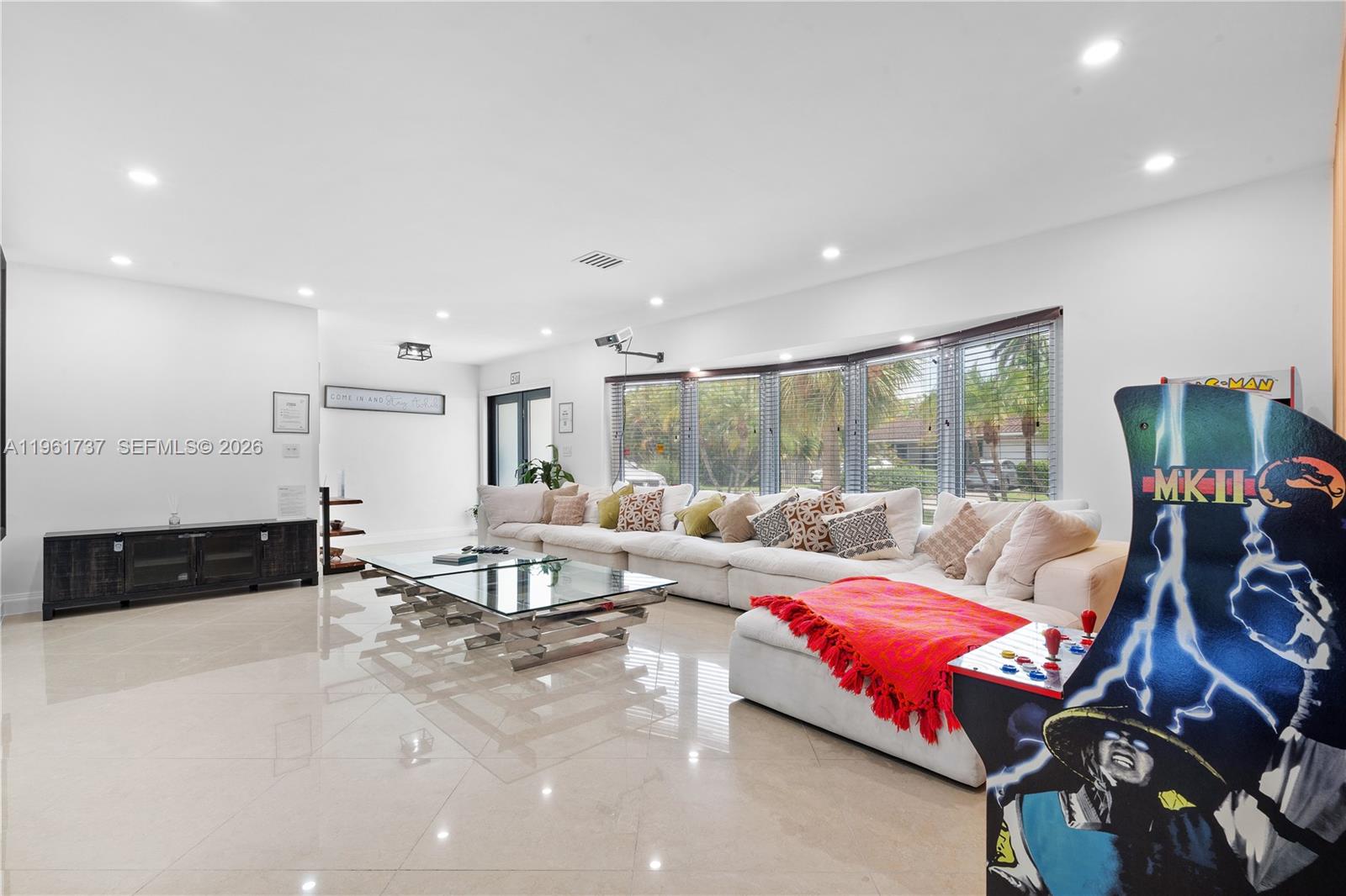 A spacious living room features a large white sectional sofa, glass coffee table, and arcade game — 1144 Adams St, Hollywood FL 33019, HOLLYWOOD, FL