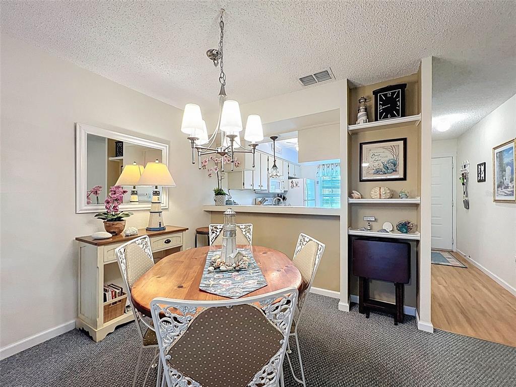 A dining room features a round wooden table, white metal chairs, and built-in wall shelving — 6433 TINA DRIVE UNIT 12, NEW PORT RICHEY, FL