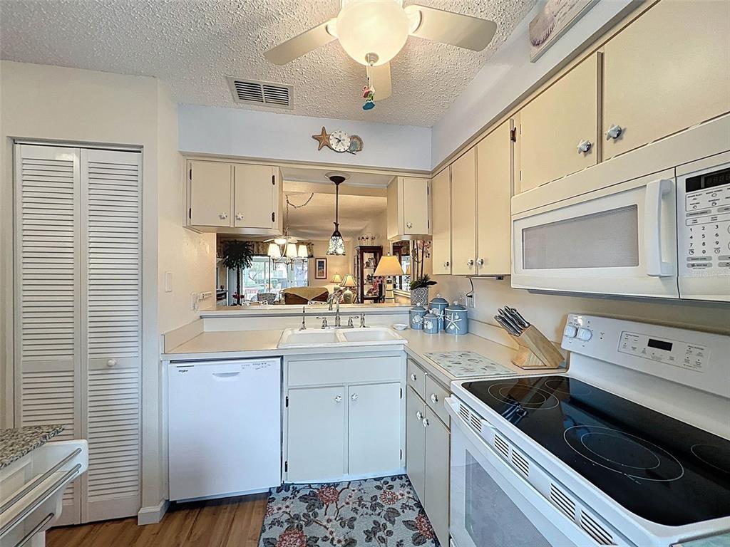 A kitchen features white appliances, light-colored cabinets, a double sink, and a pass-through window — 6433 TINA DRIVE UNIT 12, NEW PORT RICHEY, FL