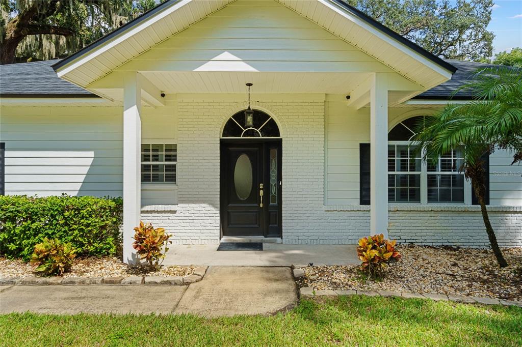 The exterior of a white house features a covered porch, brick facade, and dark door — 715 MAGNOLIA STREET, WINDERMERE, FL