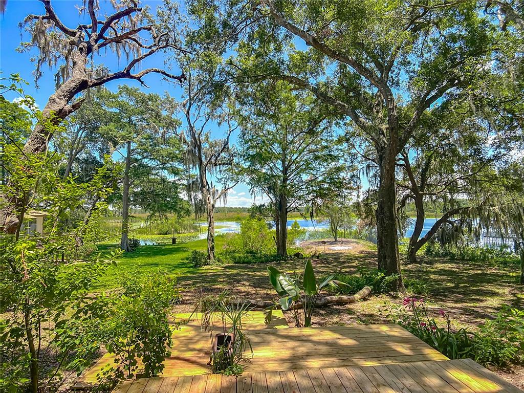 A wooden deck overlooks a grassy yard with mature trees leading to a lake — 8781 S LAKESHORE DRIVE, FLORAL CITY, FL