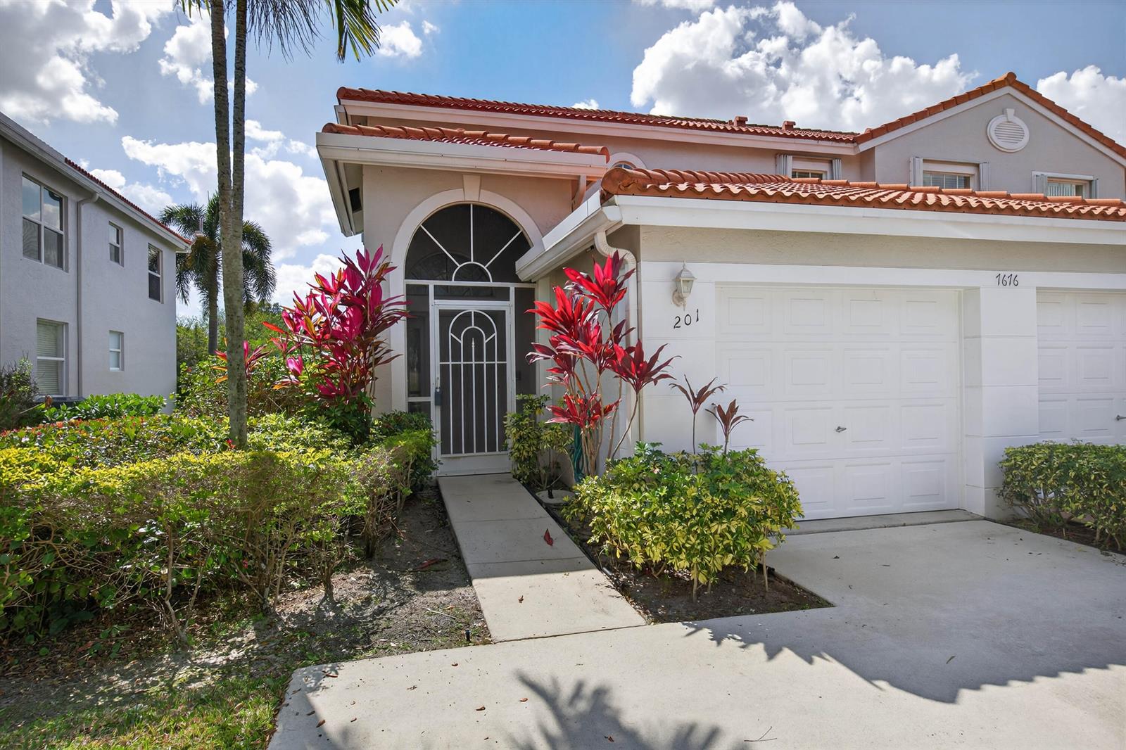 A residential building exterior features a white garage, a front entryway, and tropical landscaping — 7676 Springwater Place # 201, Boynton Beach FL 33437, BOYNTON BEACH, FL