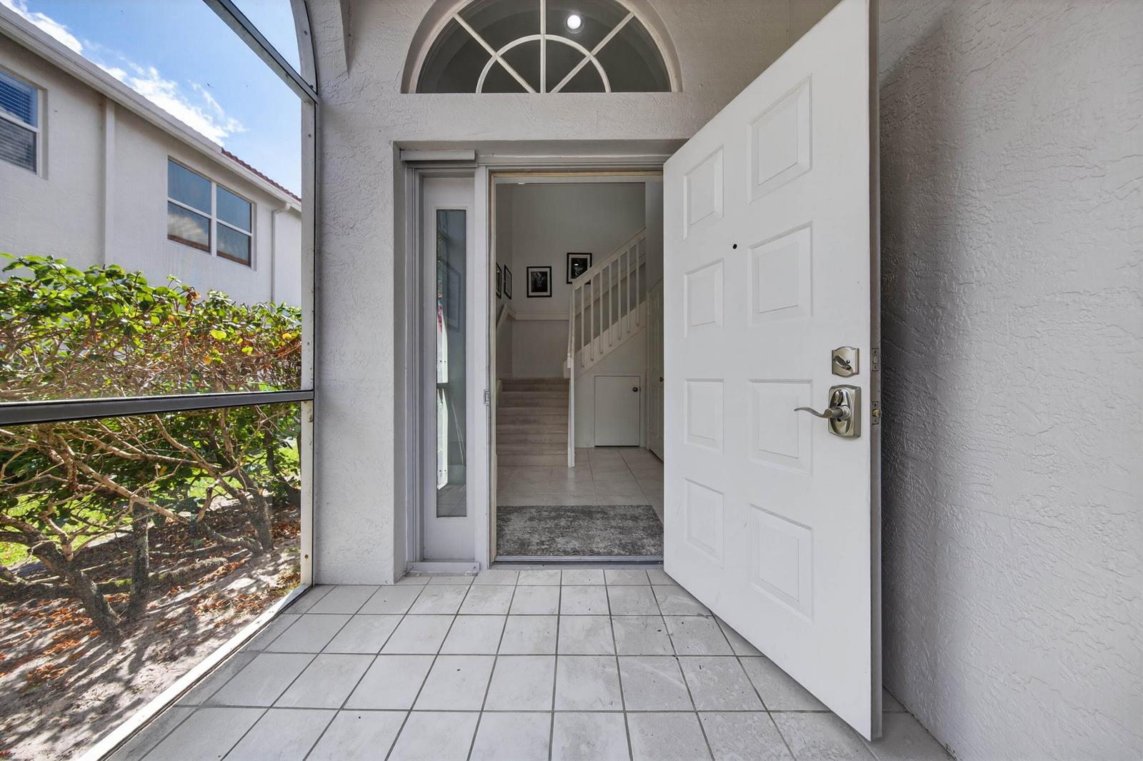 A white front door opens into a tiled entryway with a staircase and arched transom window — 7676 Springwater Place # 201, Boynton Beach FL 33437, BOYNTON BEACH, FL
