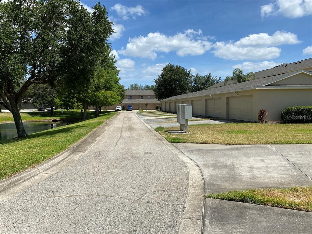 A paved driveway leads toward a row of garage doors next to a small pond — 12740 LANGSTAFF DRIVE, WINDERMERE, FL