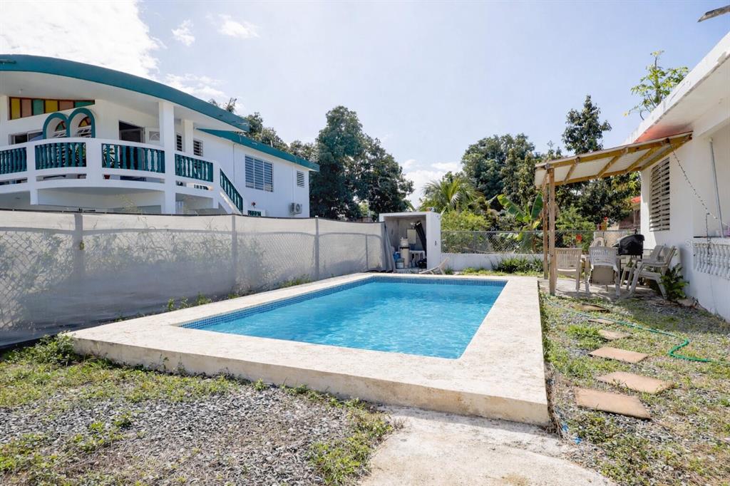 A rectangular swimming pool with a stone deck sits in a backyard with a house — 2244 REPARTO MATIAS, RINCON, PR