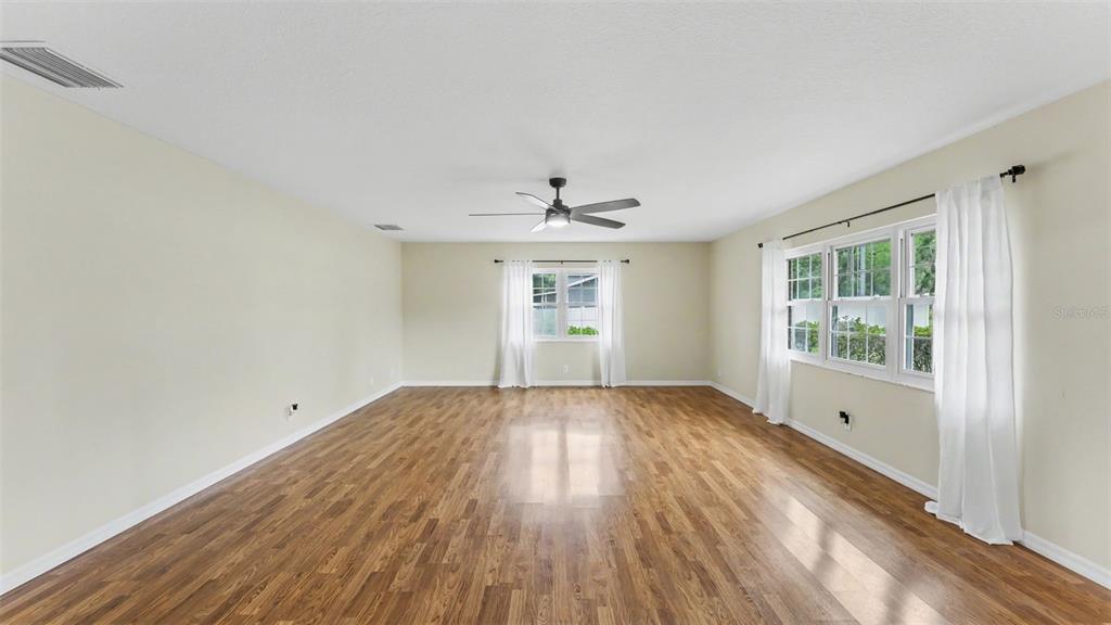 A spacious, empty room features light-colored walls, wood-look flooring, a ceiling fan, and white curtains — 2510 GIBSONIA GALLOWAY ROAD, LAKELAND, FL