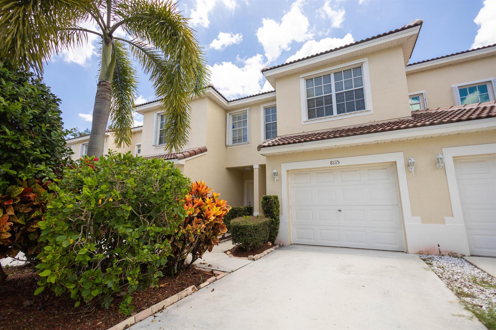 A two-story townhouse with a beige stucco exterior, a single-car garage, and a palm tree — 8115 Bellagio Lane, Boynton Beach FL 33472, BOYNTON BEACH, FL