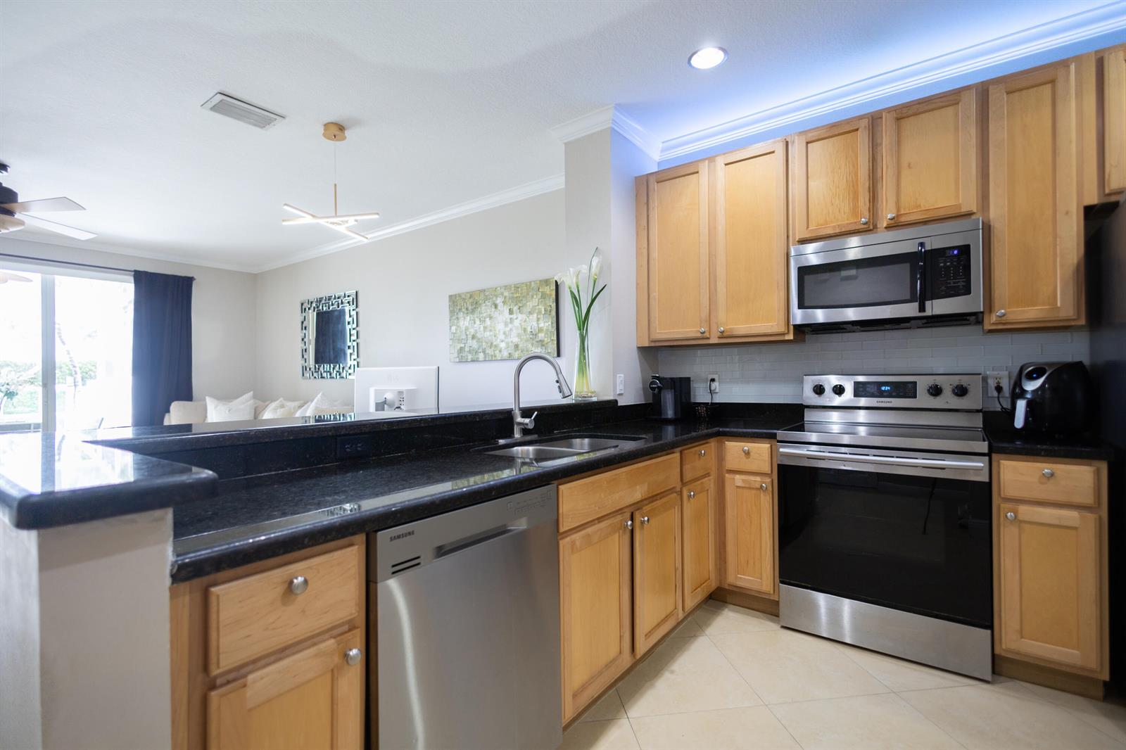 A kitchen features light wood cabinets, black granite countertops, stainless steel appliances, and tile flooring — 8115 Bellagio Lane, Boynton Beach FL 33472, BOYNTON BEACH, FL