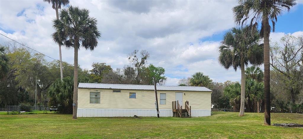 A single-story mobile home with light yellow siding sits on a grassy lot with palms — 2122 CR 426, LAKE PANASOFFKEE, FL