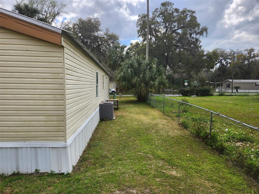 The side exterior of a mobile home features light siding, a central air unit, and fencing — 2122 CR 426, LAKE PANASOFFKEE, FL