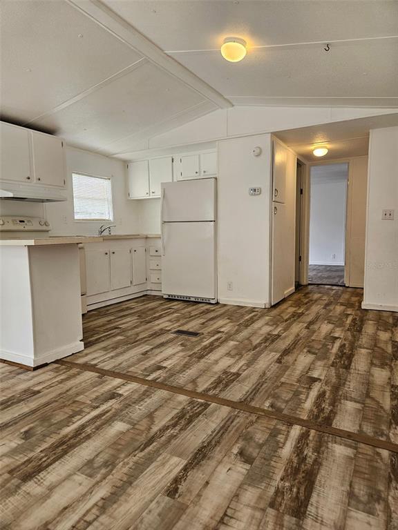 A kitchen with white cabinets, white appliances, and wood-look flooring leads to a hallway — 2122 CR 426, LAKE PANASOFFKEE, FL