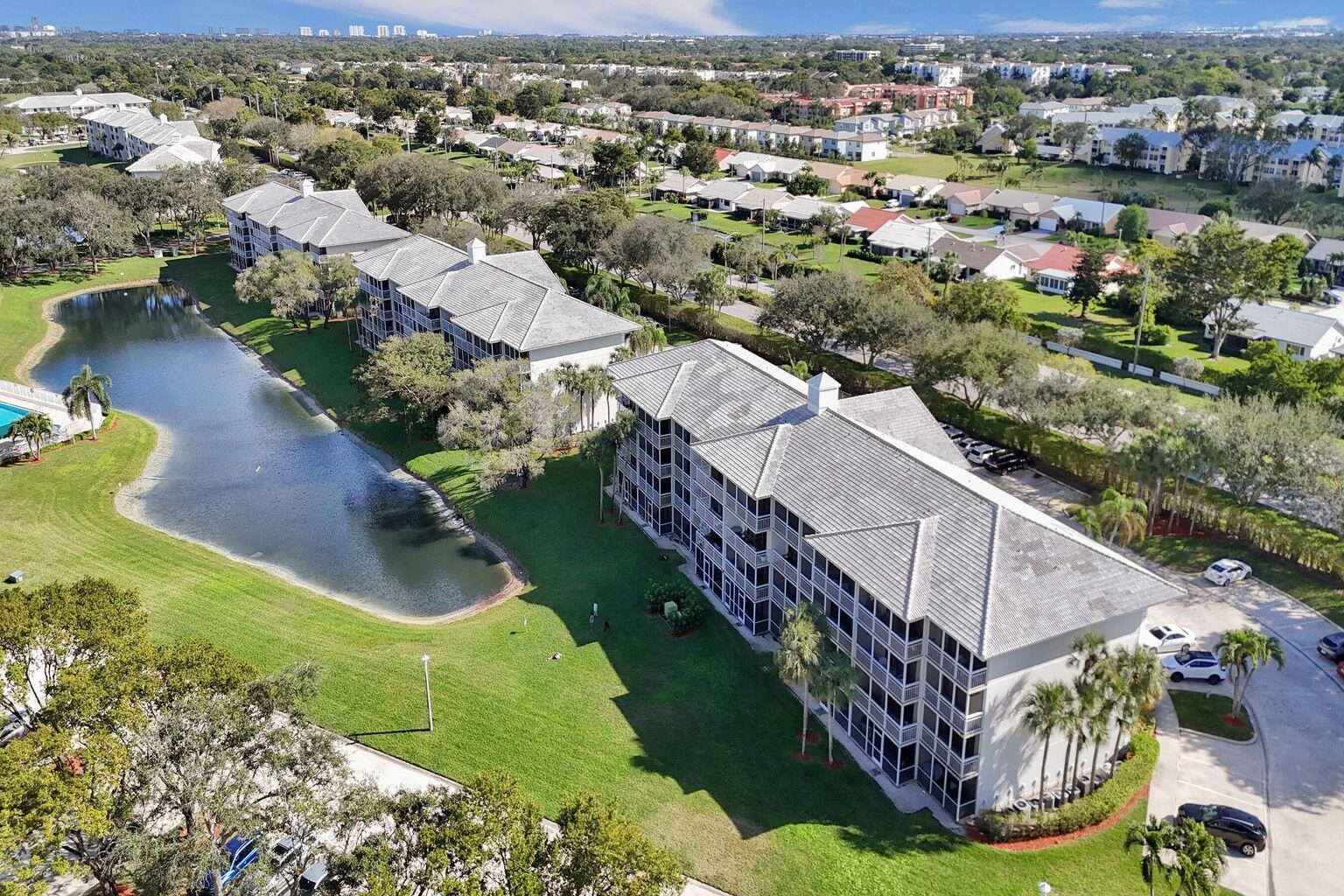An aerial view shows multi-story apartment buildings situated next to a pond and green lawn — 6193 Balboa Circle # 201, Boca Raton FL 33433, BOCA RATON, FL