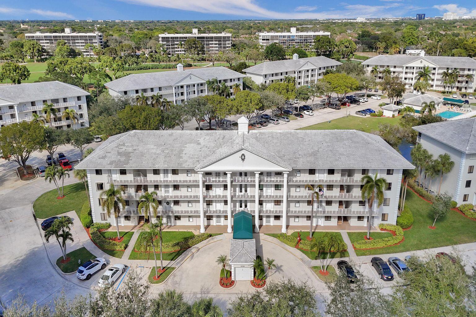 An aerial view of a multi-story apartment building with a green entrance canopy and parking — 6193 Balboa Circle # 201, Boca Raton FL 33433, BOCA RATON, FL
