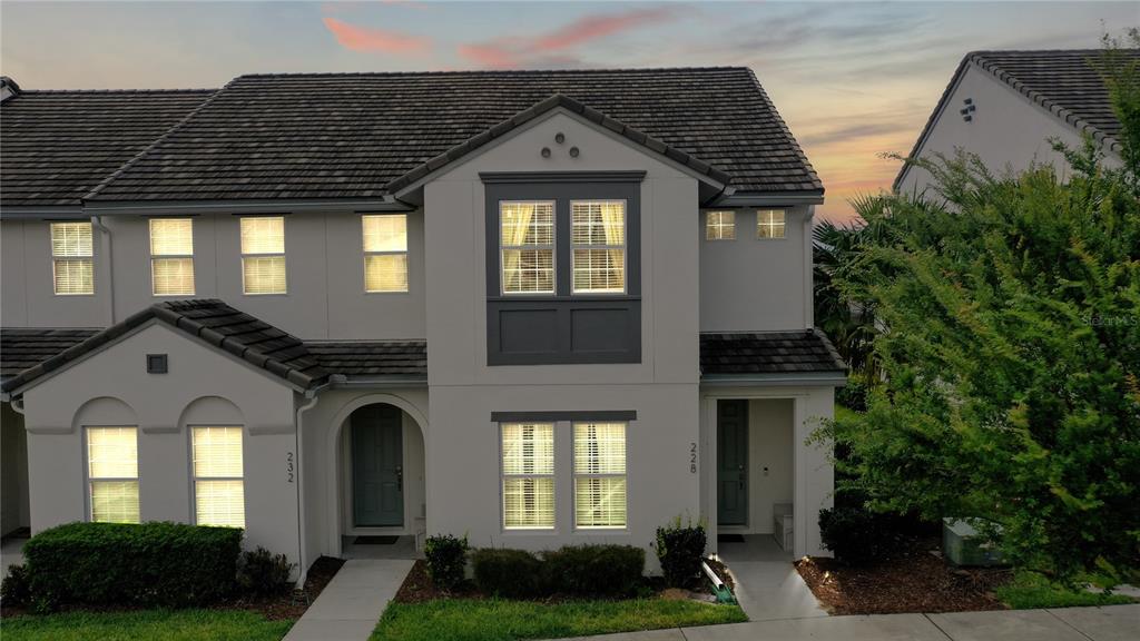 The exterior of a two-story townhouse features a gray stucco facade, dark roof tiles, and windows — 228 CAPTIVA DR, DAVENPORT, FL