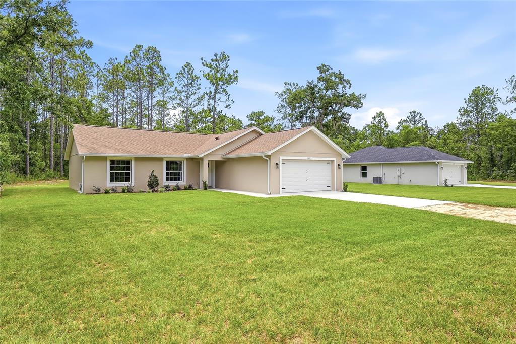 A tan, single-story house with a two-car garage sits on a large, grassy lot — 16325 FORCE ROAD, BROOKSVILLE, FL