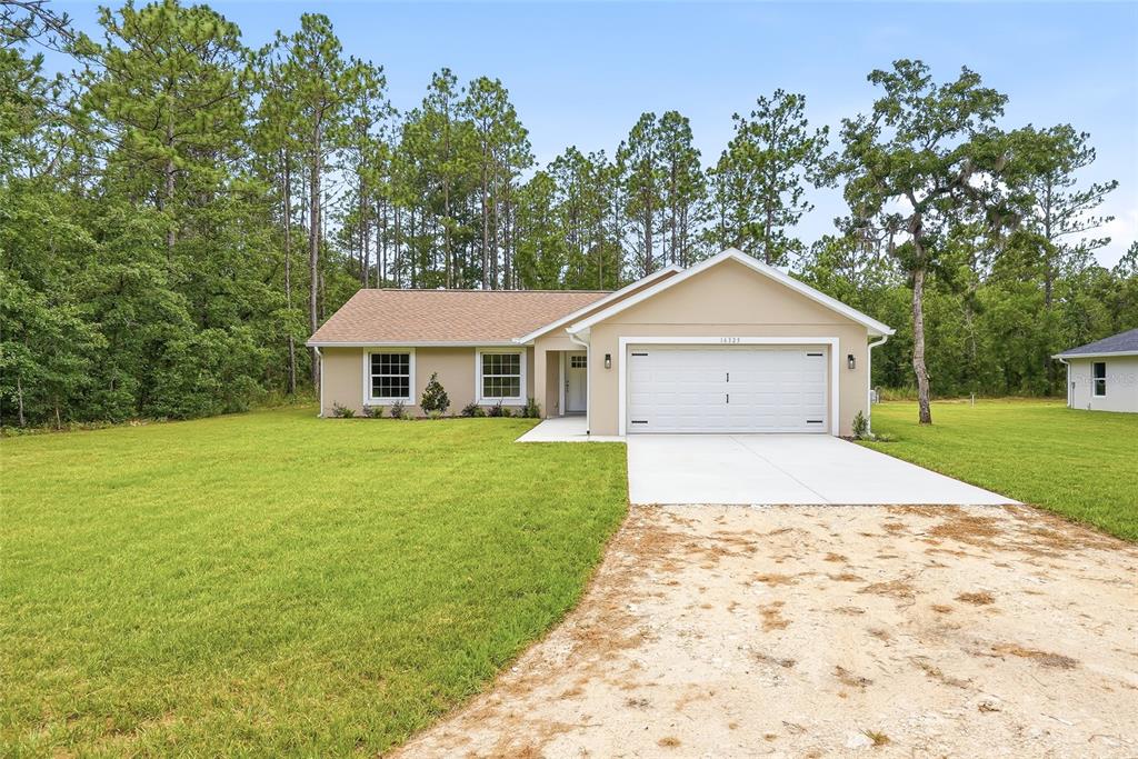 A single-story house with a tan exterior, white garage door, and a concrete driveway — 16325 FORCE ROAD, BROOKSVILLE, FL
