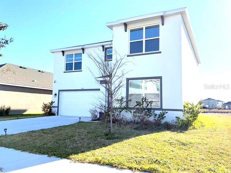 A two-story white stucco house features a garage and a small front yard — 2785 GARDINER LANE, ZEPHYRHILLS, FL