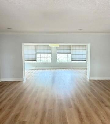 An empty room with light wood flooring and a large opening to a sunroom — 3230 Aqua Vista Drive, Pompano Beach FL 33062, POMPANO BEACH, FL