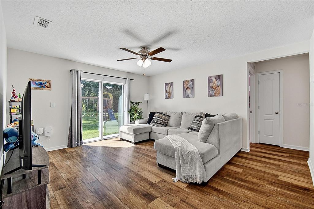 A living room features a gray sectional sofa, wood-look flooring, and sliding glass doors — 70 PEBBLE BEACH DRIVE, PALM COAST, FL