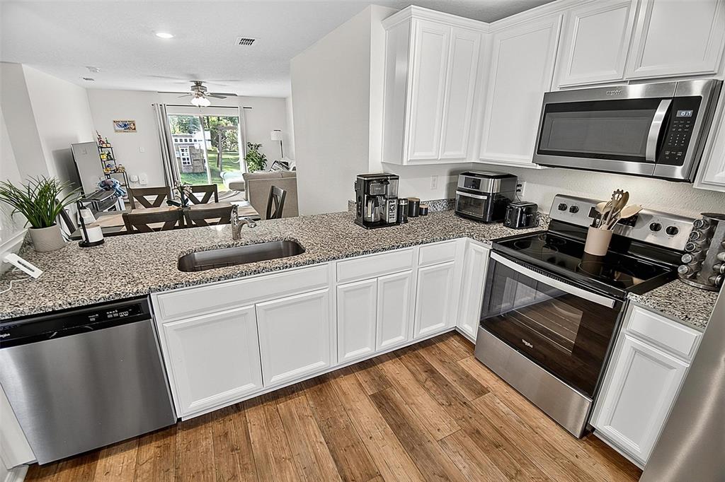 A kitchen features white cabinets, granite countertops, stainless steel appliances, and wood-look flooring — 70 PEBBLE BEACH DRIVE, PALM COAST, FL