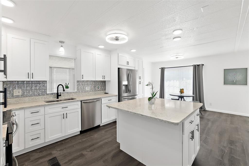 A modern kitchen features white cabinets, a granite-topped island, stainless steel appliances, and dark flooring — 5660 WOOD STREET, PORT ORANGE, FL