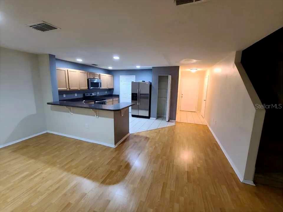 A kitchen with light wood cabinets and stainless steel appliances overlooks a hardwood-floored living area — 1034 CHALCEDONY STREET, KISSIMMEE, FL