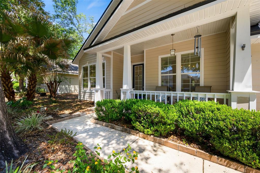 A tan house exterior features a covered front porch with white railings and landscaping — 2117 NW 144TH STREET, NEWBERRY, FL