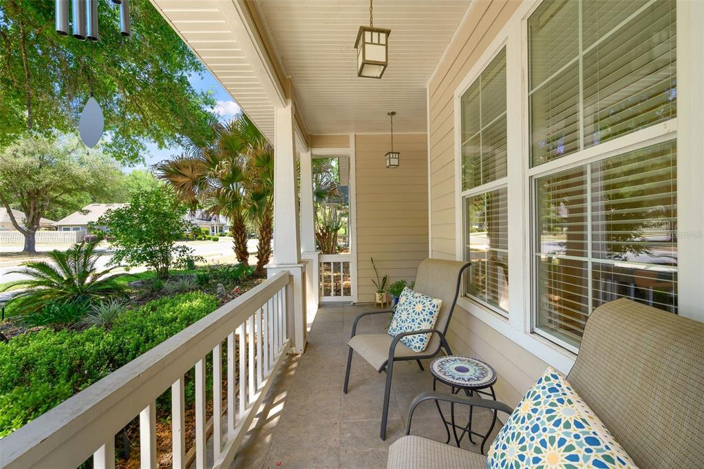 A covered front porch features a white railing, two chairs with patterned pillows, and tile flooring — 2117 NW 144TH STREET, NEWBERRY, FL
