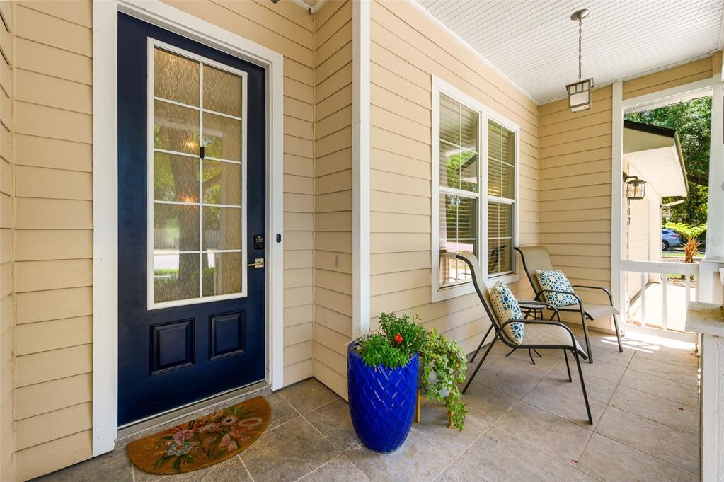 A covered front porch features a dark blue door, beige siding, and two patio chairs — 2117 NW 144TH STREET, NEWBERRY, FL