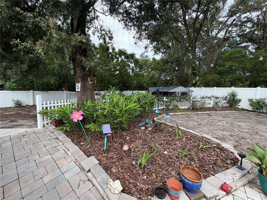 A backyard garden bed features mulch, decorative metal flowers, and a large tree — 4819 BIRCHMONT PLACE, ORLANDO, FL