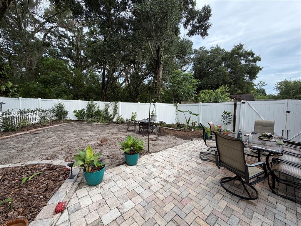 A backyard features a brick paver patio with dining furniture, potted plants, and a white fence — 4819 BIRCHMONT PLACE, ORLANDO, FL
