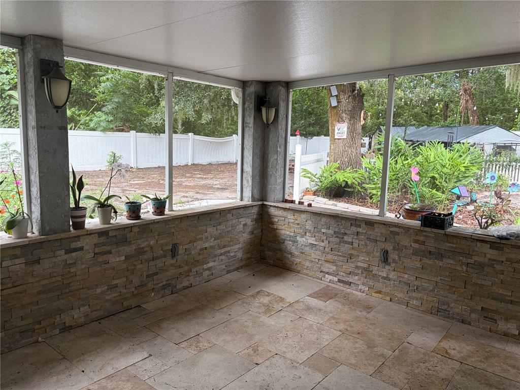 A screened-in porch with stone veneer walls, travertine tile flooring, and views of a backyard — 4819 BIRCHMONT PLACE, ORLANDO, FL