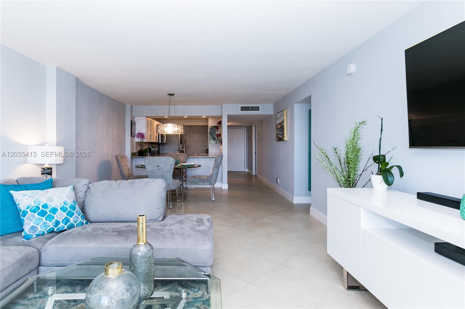 A living room with a grey sectional, glass coffee table, and an adjacent dining area — 14 Royal Palm Way # 601, Boca Raton FL 33432, BOCA RATON, FL