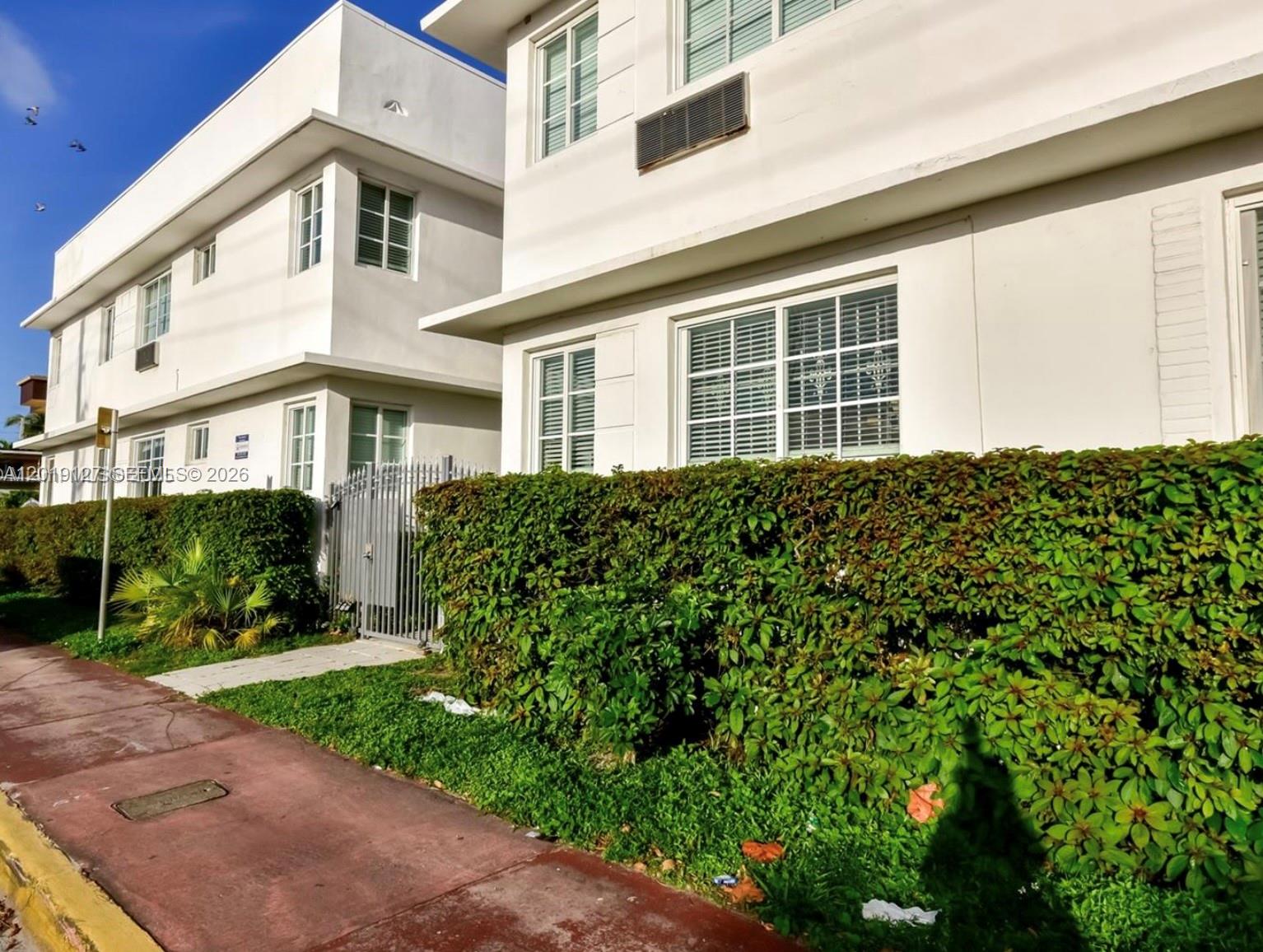 Two white two-story buildings are separated by a metal gate and a green hedge — 8415 Harding Ave # 14, Miami Beach FL 33141, MIAMI BEACH, FL