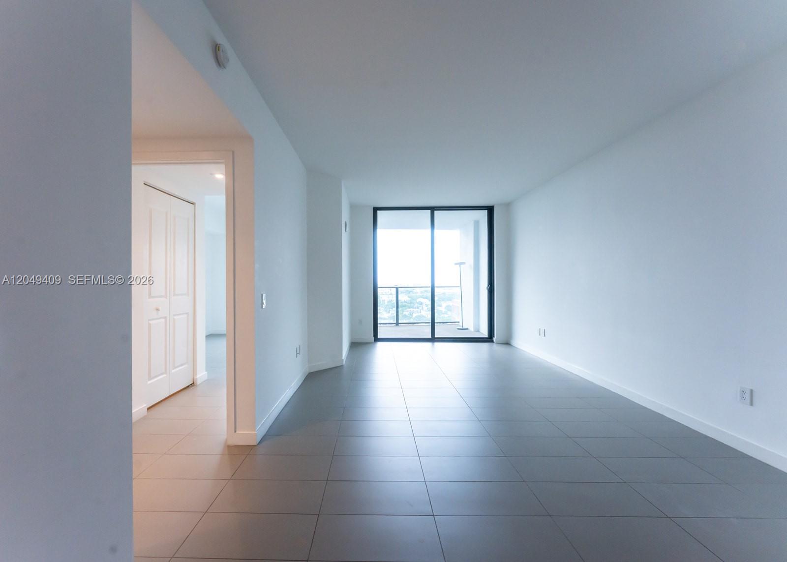An empty room with gray tile flooring and a sliding glass door leading to a balcony — 1600 NE 1st Ave # 1814, Miami FL 33132, MIAMI, FL