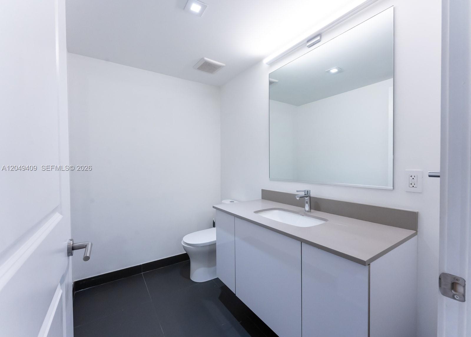 A modern bathroom features a white vanity with a gray countertop, mirror, and dark flooring — 1600 NE 1st Ave # 1814, Miami FL 33132, MIAMI, FL