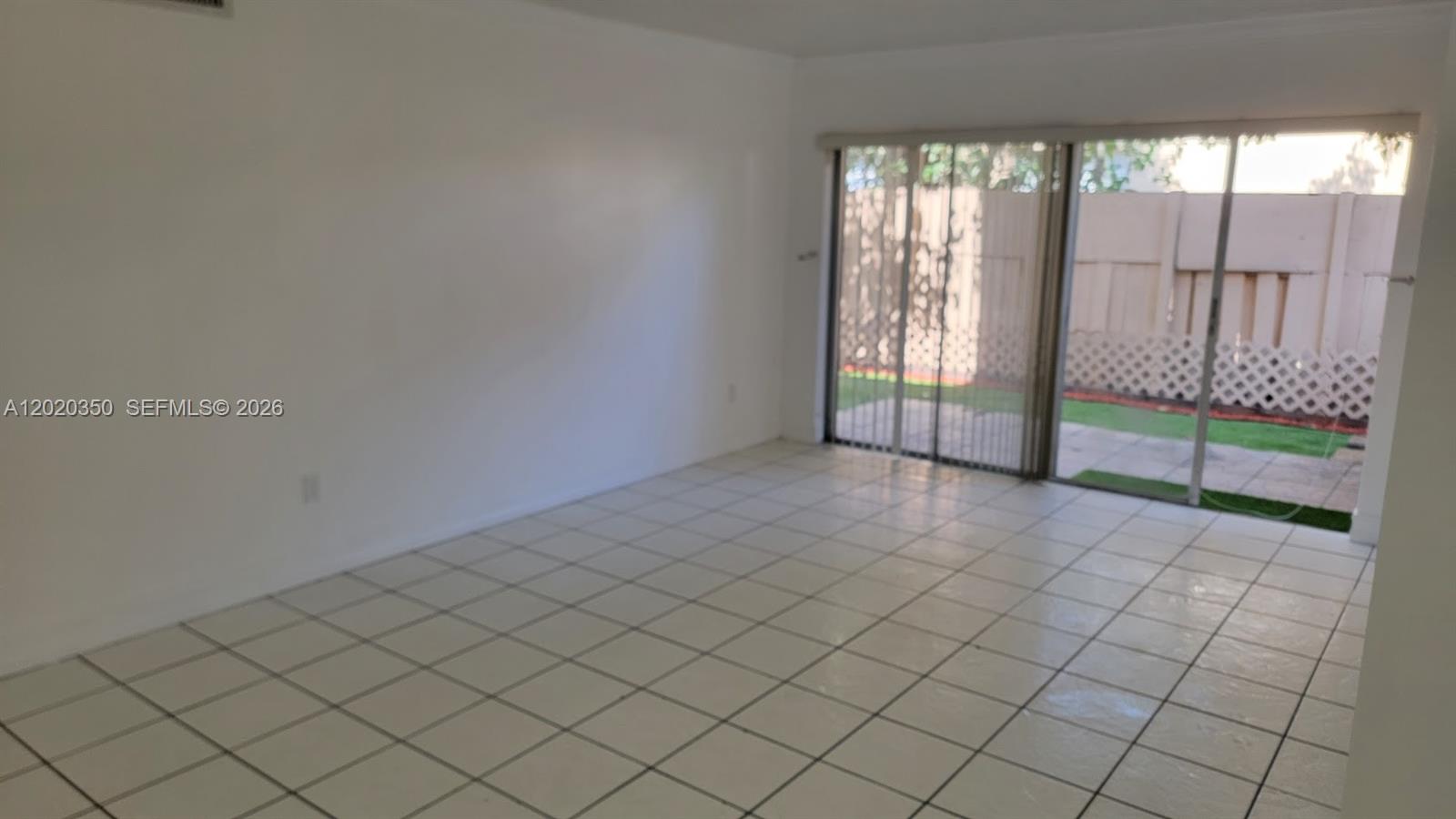 An empty room features white tiled floors and a sliding glass door leading to a patio — 4410 NW 79th Ave # 1C, Doral FL 33166, DORAL, FL
