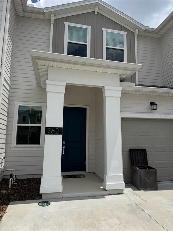 A two-story house exterior features light gray siding, a dark blue front door, and white columns — 7621 DANUBE ROAD, KISSIMMEE, FL
