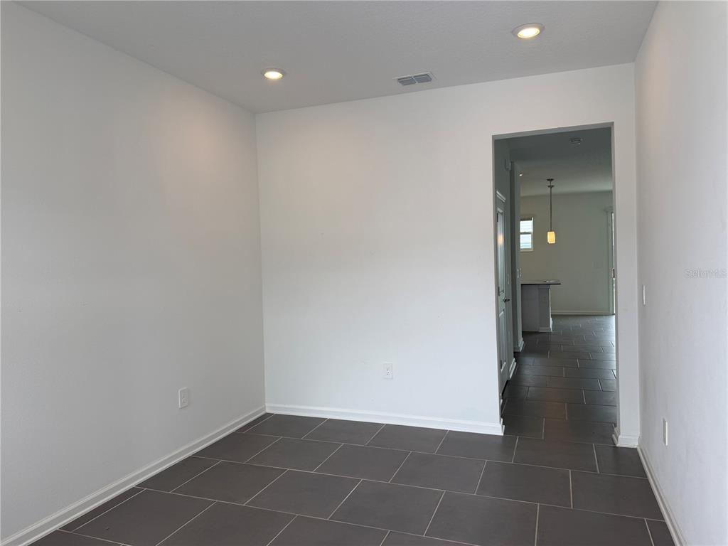 An empty room with white walls, dark tile flooring, and recessed ceiling lights — 7621 DANUBE ROAD, KISSIMMEE, FL