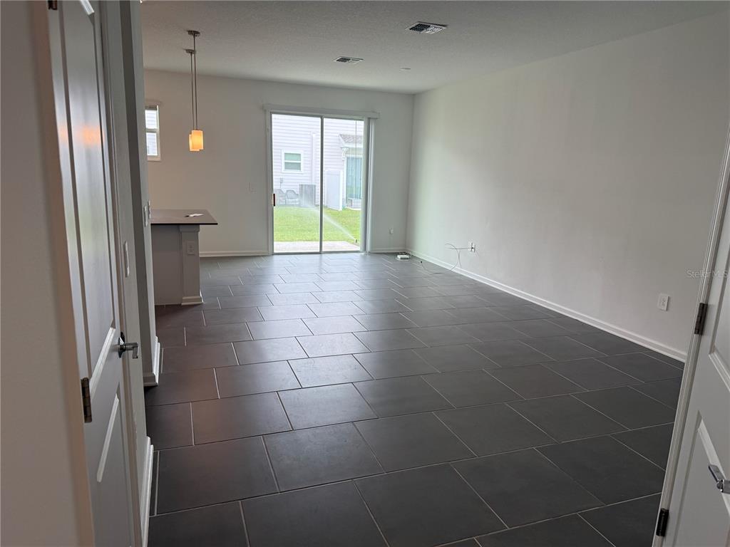 An open-concept living area features dark gray tile flooring, white walls, and a sliding glass door — 7621 DANUBE ROAD, KISSIMMEE, FL